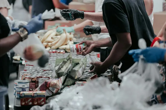 Volunteers' gloved hands sort donated food at a long table.