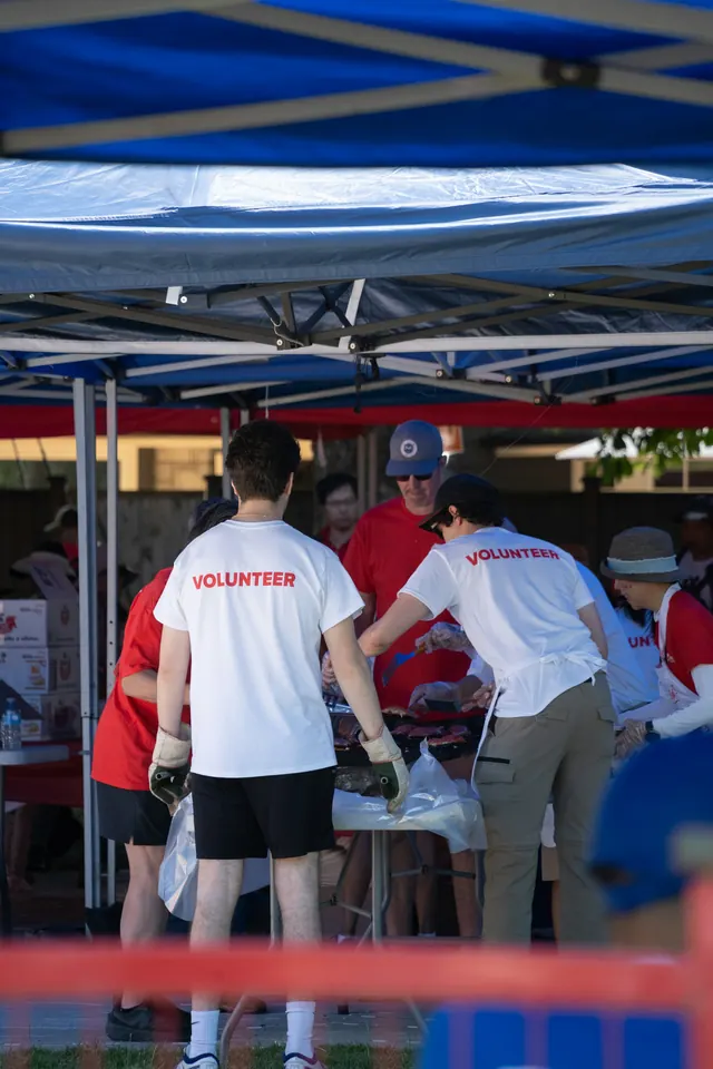 Volunteers in matching shirts organize supplies together beneath a blue canopy.