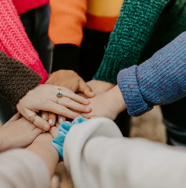 Many hands in colourful sweaters stacked together in a circle.