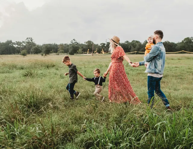 A family walks hand in hand through a sunny meadow, children leading the way.
